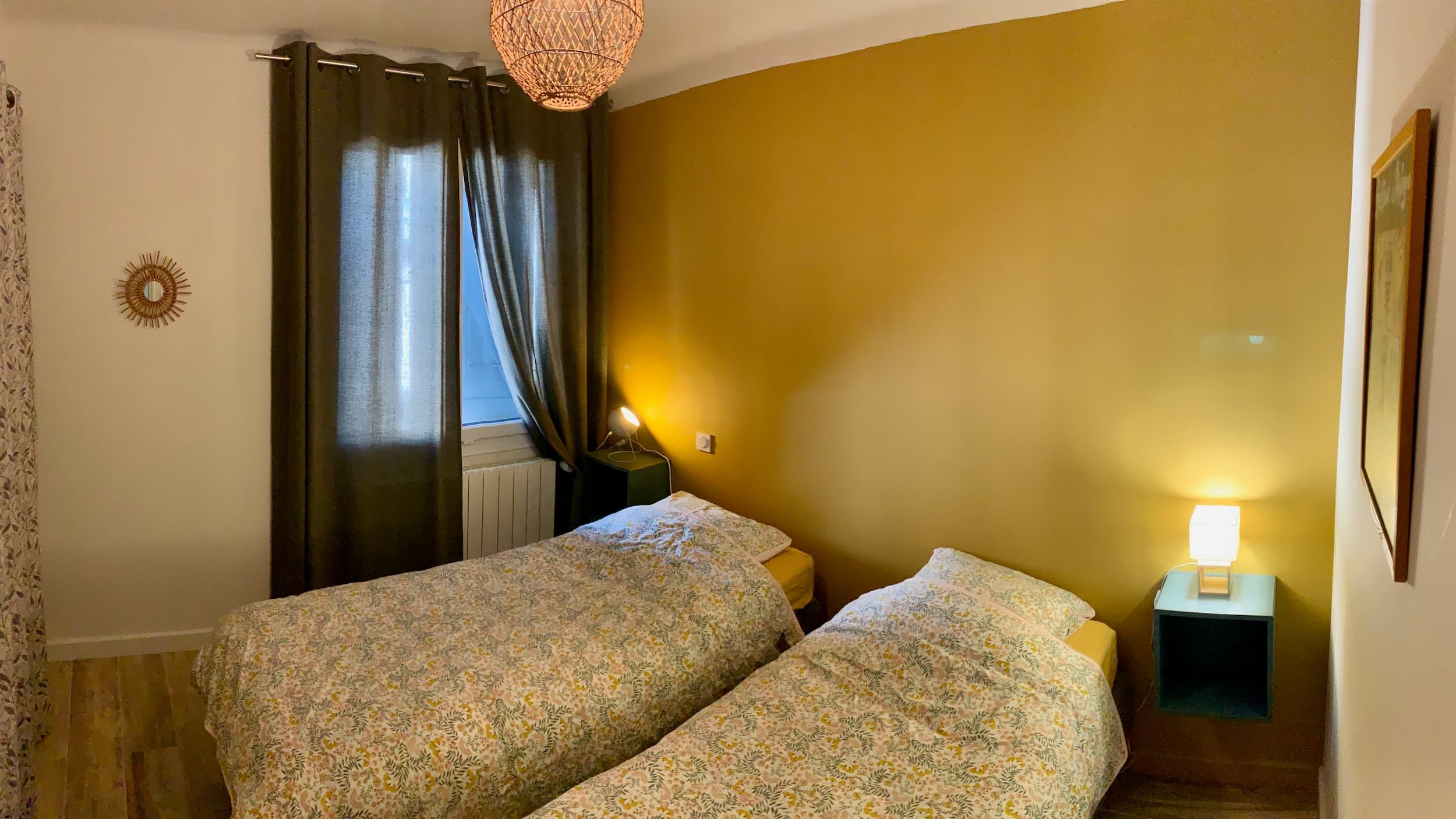 Vue de la chambre en journée avec les deux lits, le mur jaune, l'affiche, et les lampes de chevet