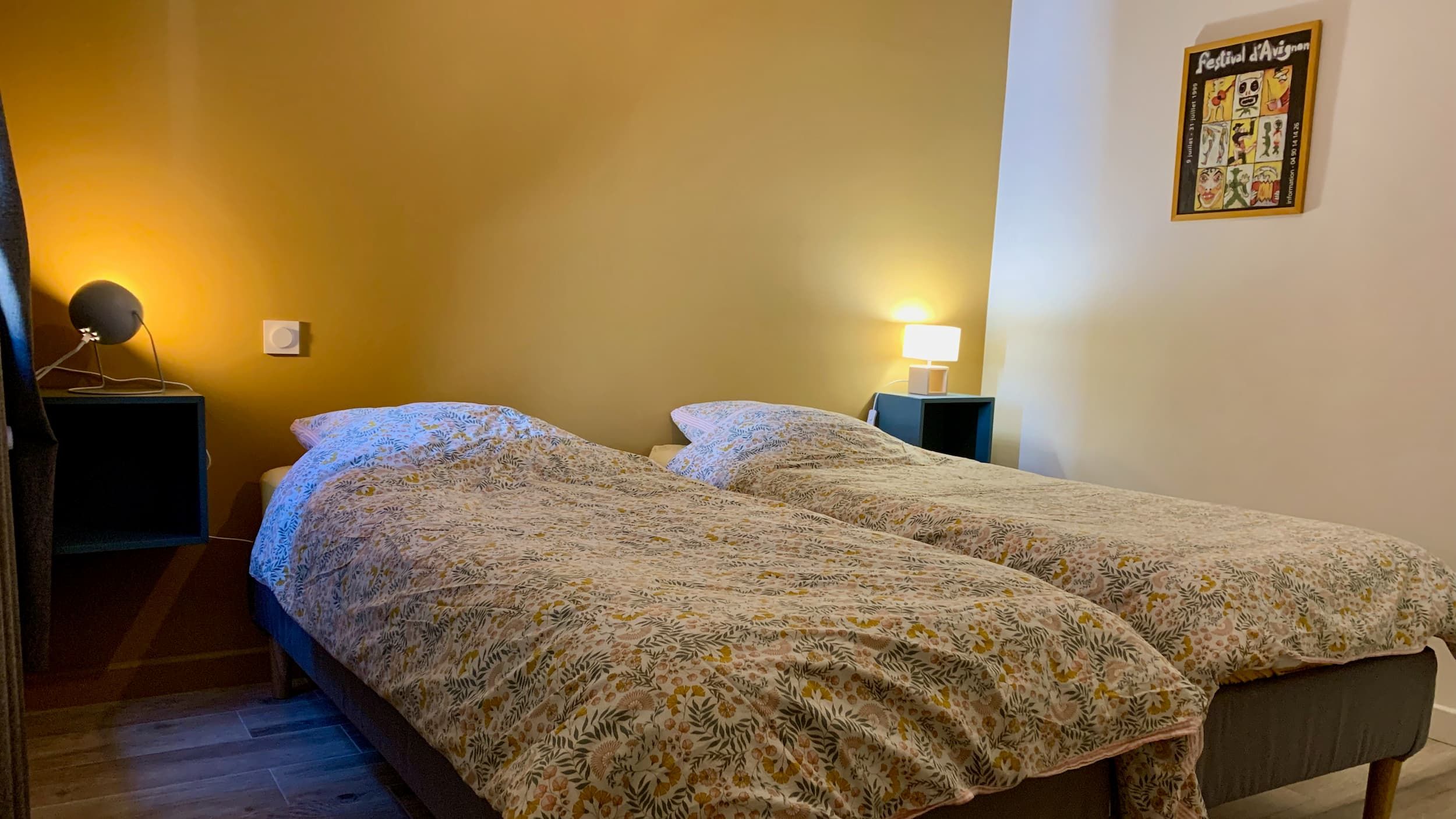 Vue de la chambre en journée avec les deux lits, le mur jaune, le mirroir, la fenêtre, et les lampes de chevet