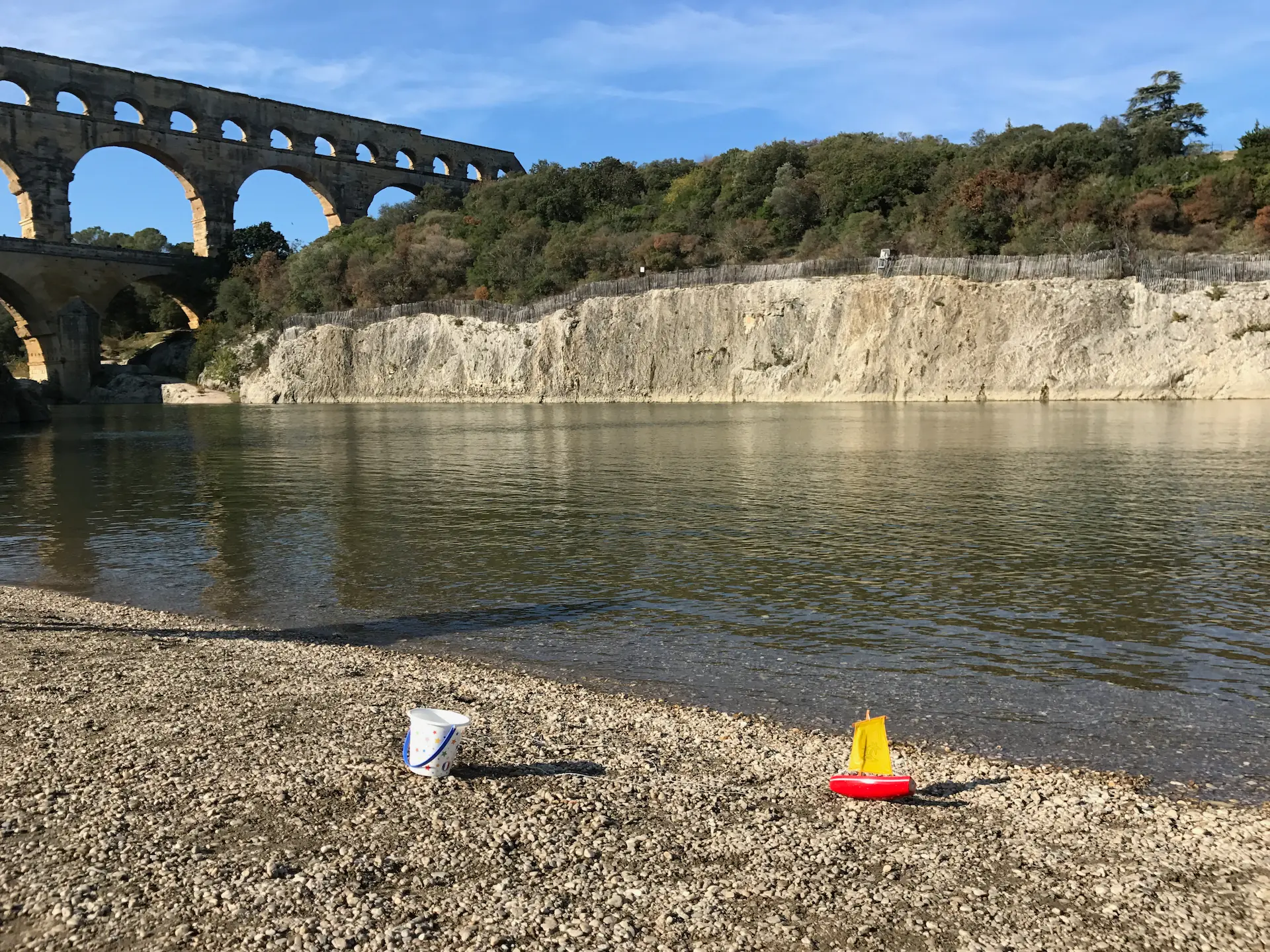 La plage de graviers au bord du Gardon devant le Pont du Gard. Des jouets d’enfant sont visibles au premier plan.