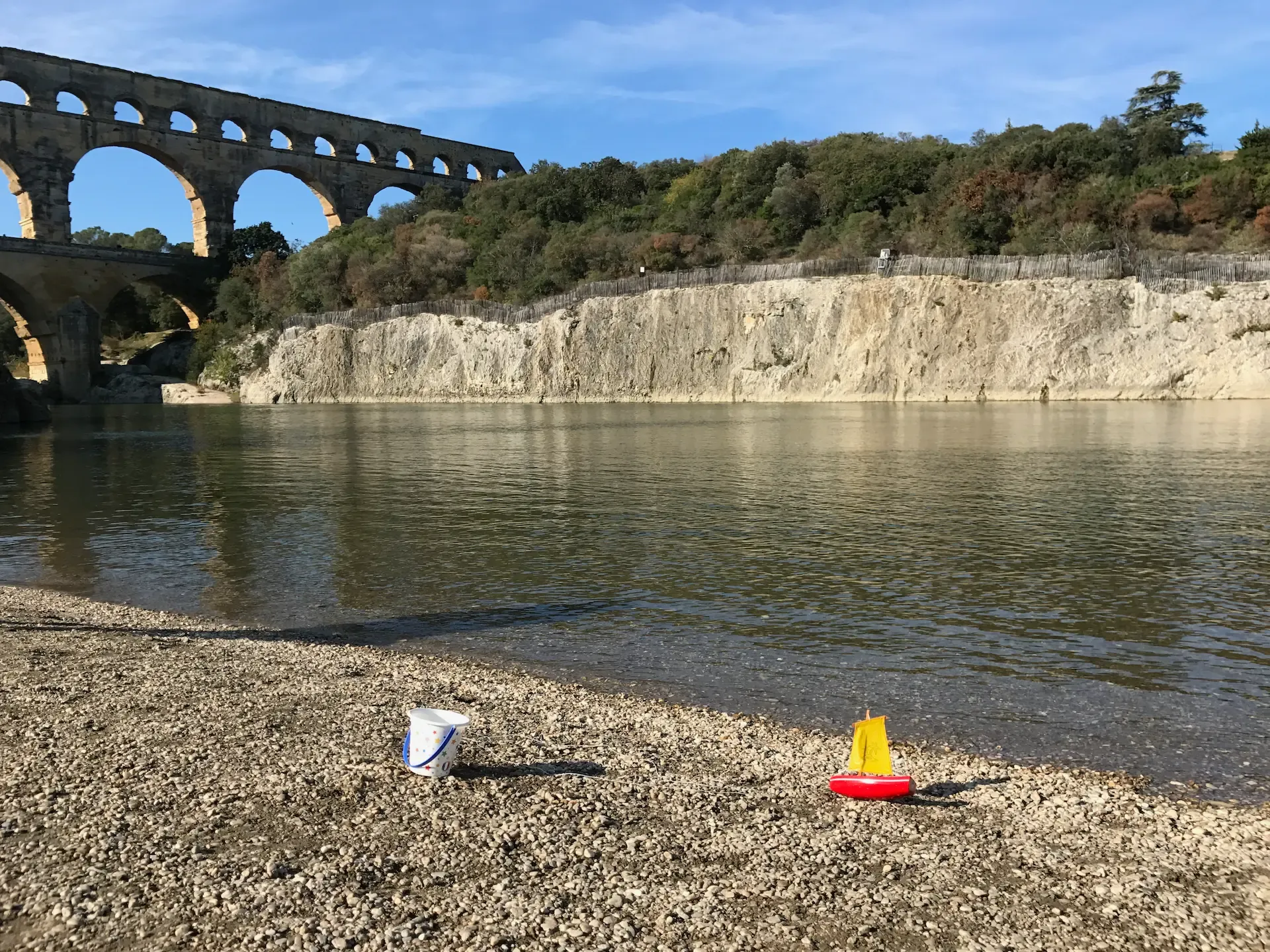 La plage de graviers au bord du Gardon devant le Pont du Gard. Des jouets d’enfant sont visibles au premier plan.