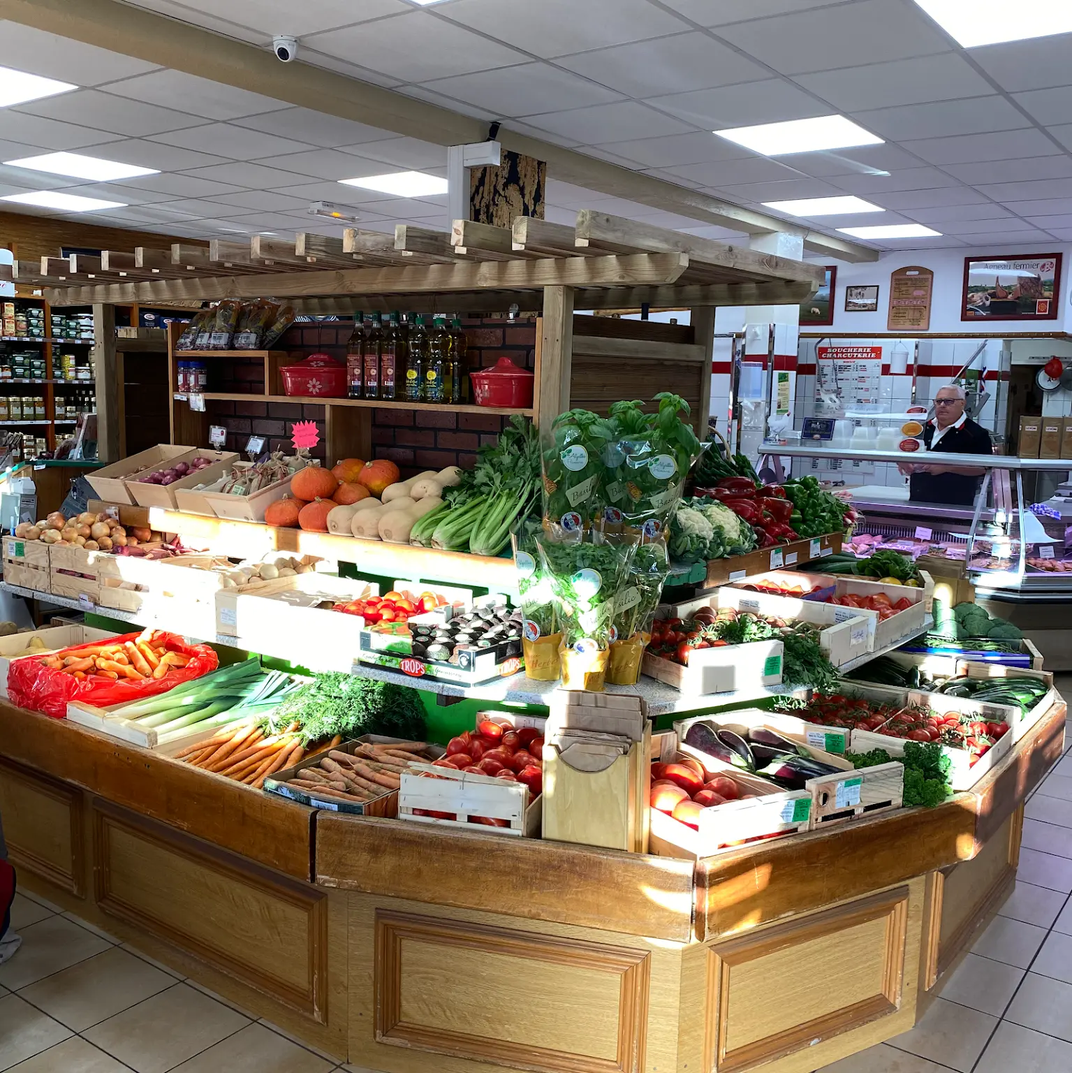 Vue de l'étal de fruits et légumes. Le patron en arrière plan dans la boucherie.