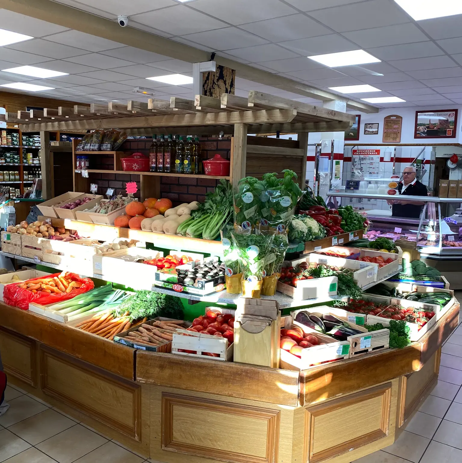 Vue de l'étal de fruits et légumes. Le patron en arrière plan dans la boucherie.